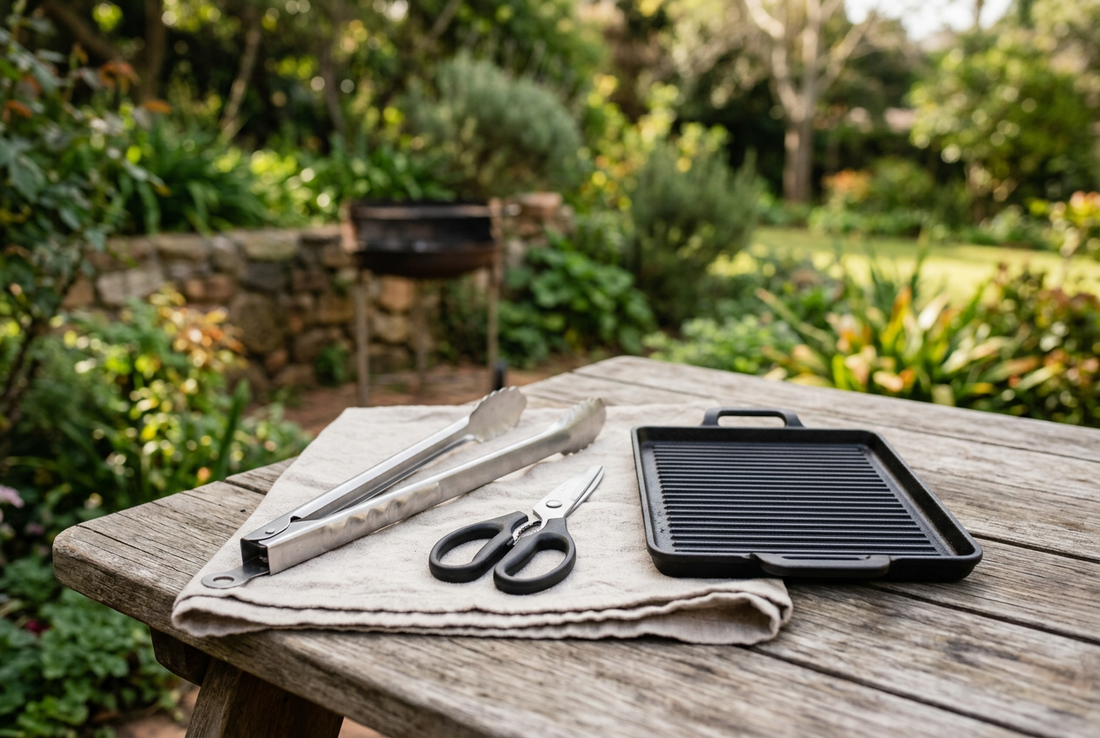Illustrative braai utensils and a grill plate arranged on an outdoor wooden table.